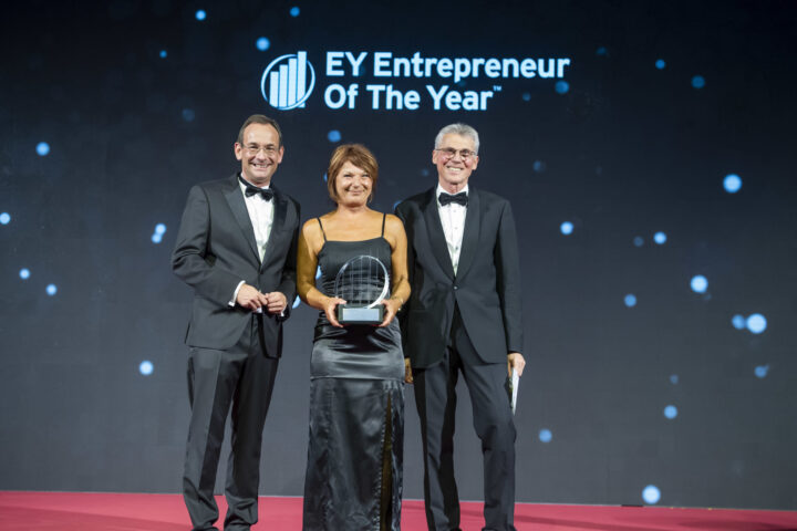 Monika Haider auf der Bühne mit dem Award in der Hand. Zwei Vertreter von EY stehen neben ihr. Im Hintergrund der Schriftzug "EY Entrepreneur Of The Year"
